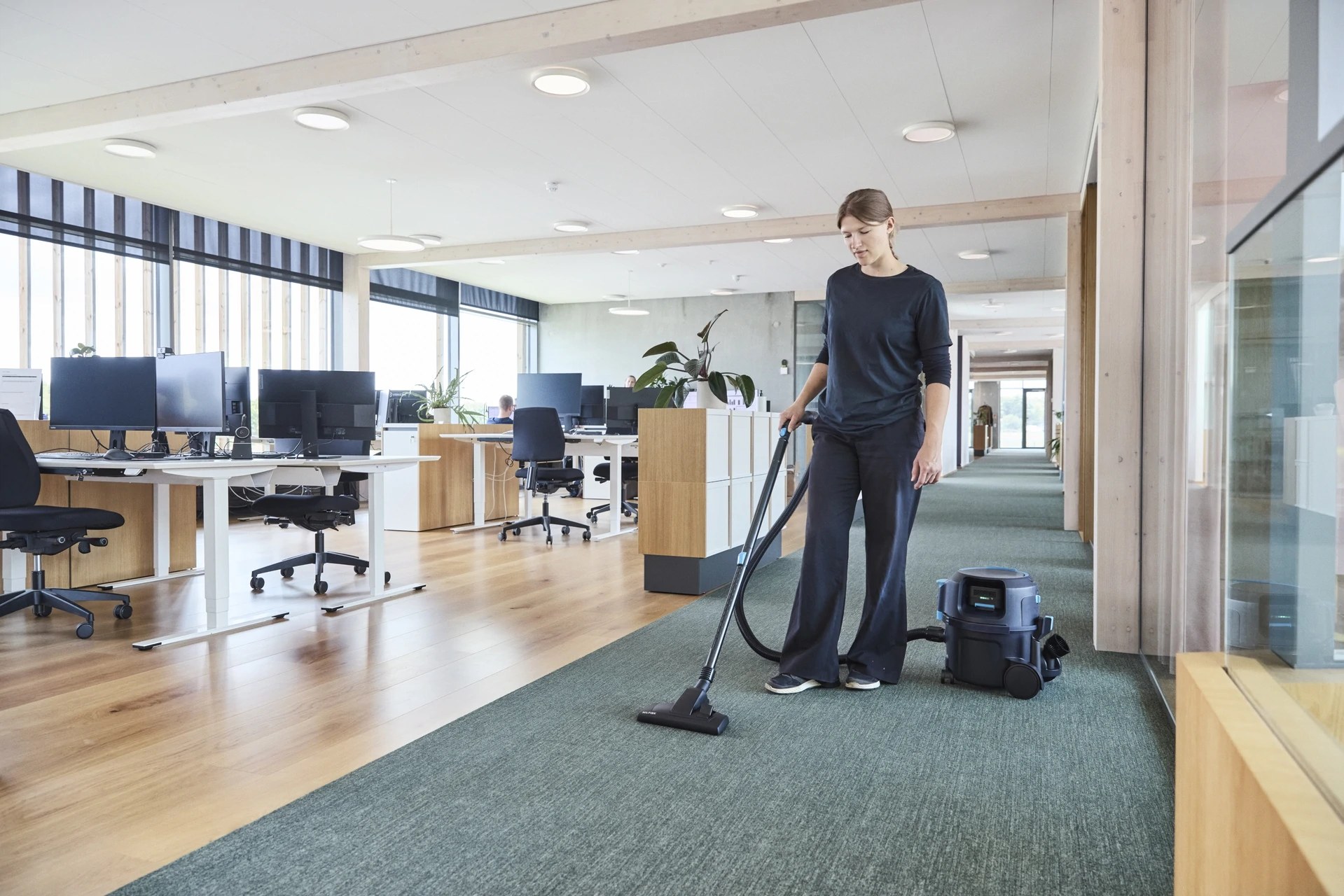Cleaner using the Nilfisk VP500 cordless canister vacuum on carpet in an open-plan office