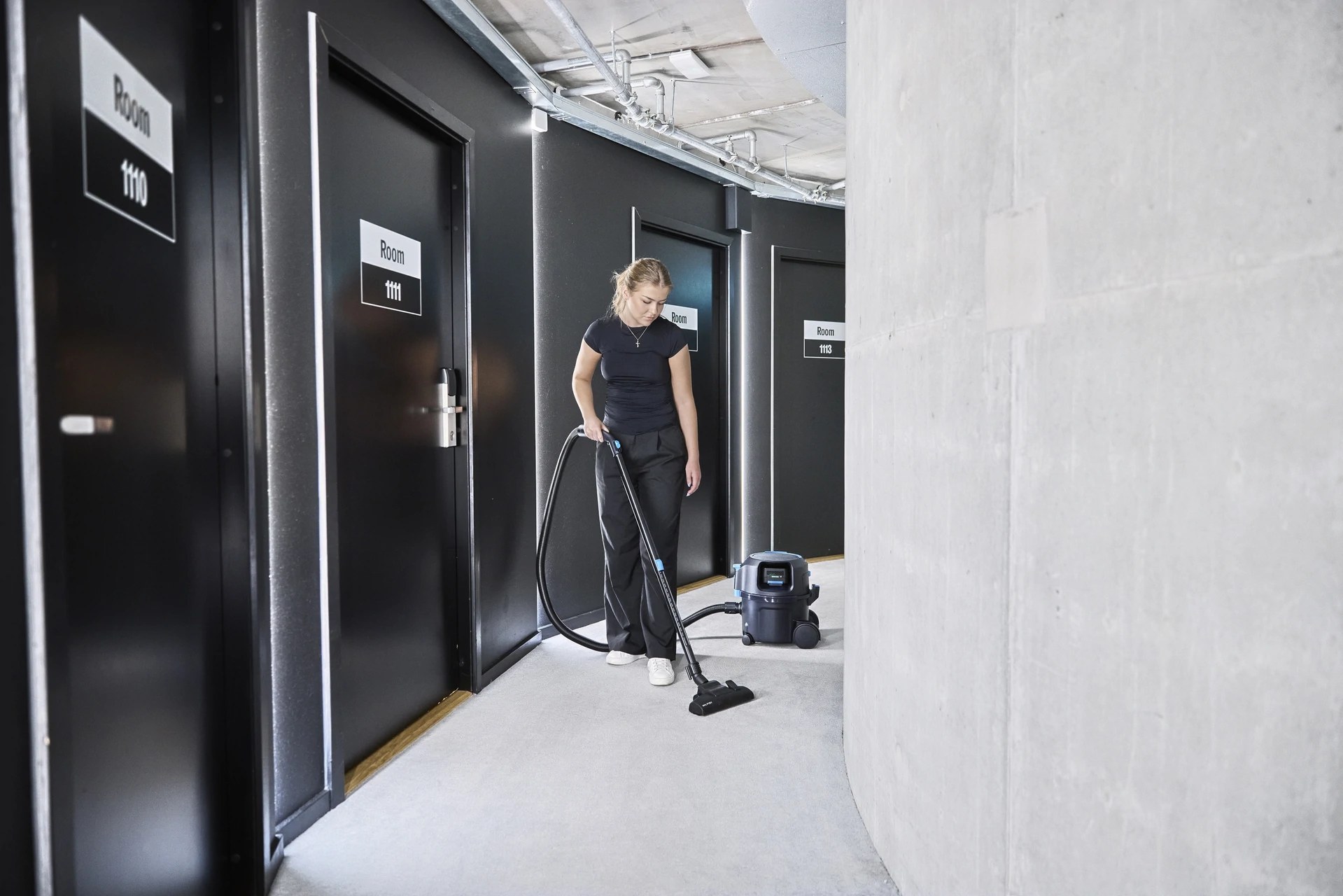 Nilfisk VP500 cordless canister vacuum in use in a hotel hallway outside guest room doors