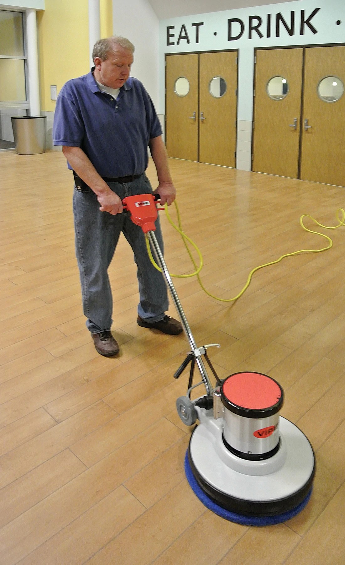 Operator running the Viper Venom VN20DS floor machine on a wood-look floor in a school cafeteria entrance