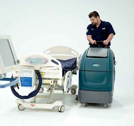 Operator standing on the Nobles Speed Scrub 350 stand-on scrubber in a hospital room setting