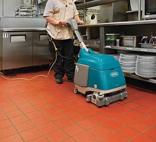 Operator scrubbing a red quarry tile kitchen floor with the corded Tennant T1