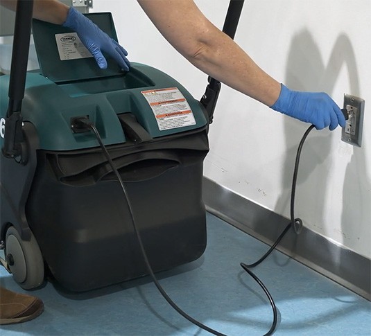 Operator plugging the Tennant S6 on-board charger into a wall outlet