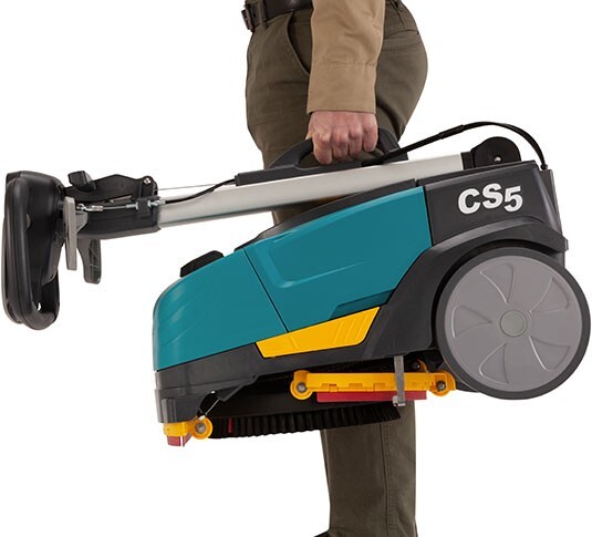 Operator carrying the Tennant CS5 with the handle folded for storage