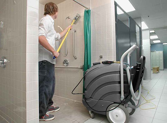 Operator cleaning a shower stall with the Tennant ASC-15 spray wand