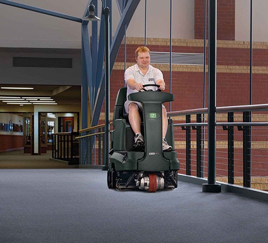 Operator riding a Nobles Strive Rider through a carpeted campus building