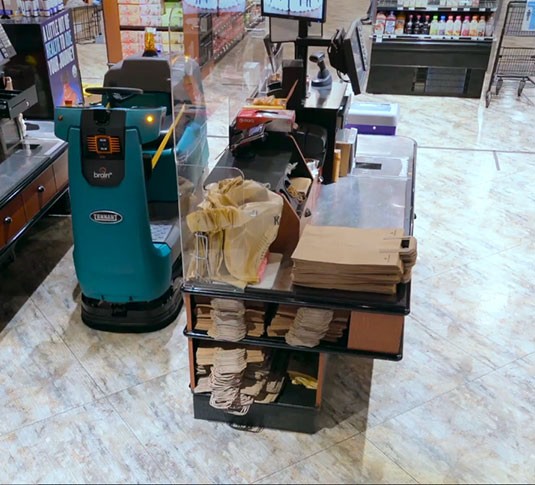 Tennant T380AMR robotic scrubber cleaning near a checkout counter in a retail store