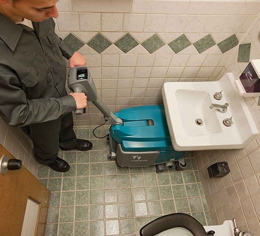 Operator cleaning a restroom floor with a Tennant T1B micro scrubber