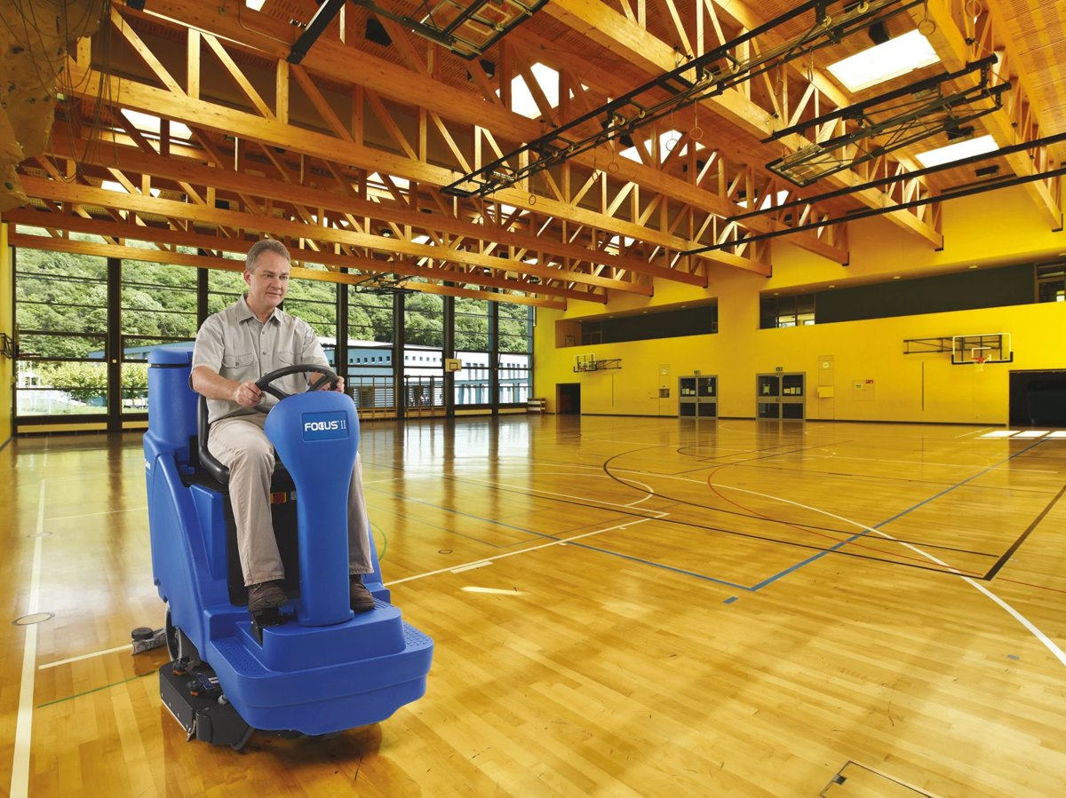 Operator scrubbing a gym floor with a Clarke Focus II BOOST rider scrubber