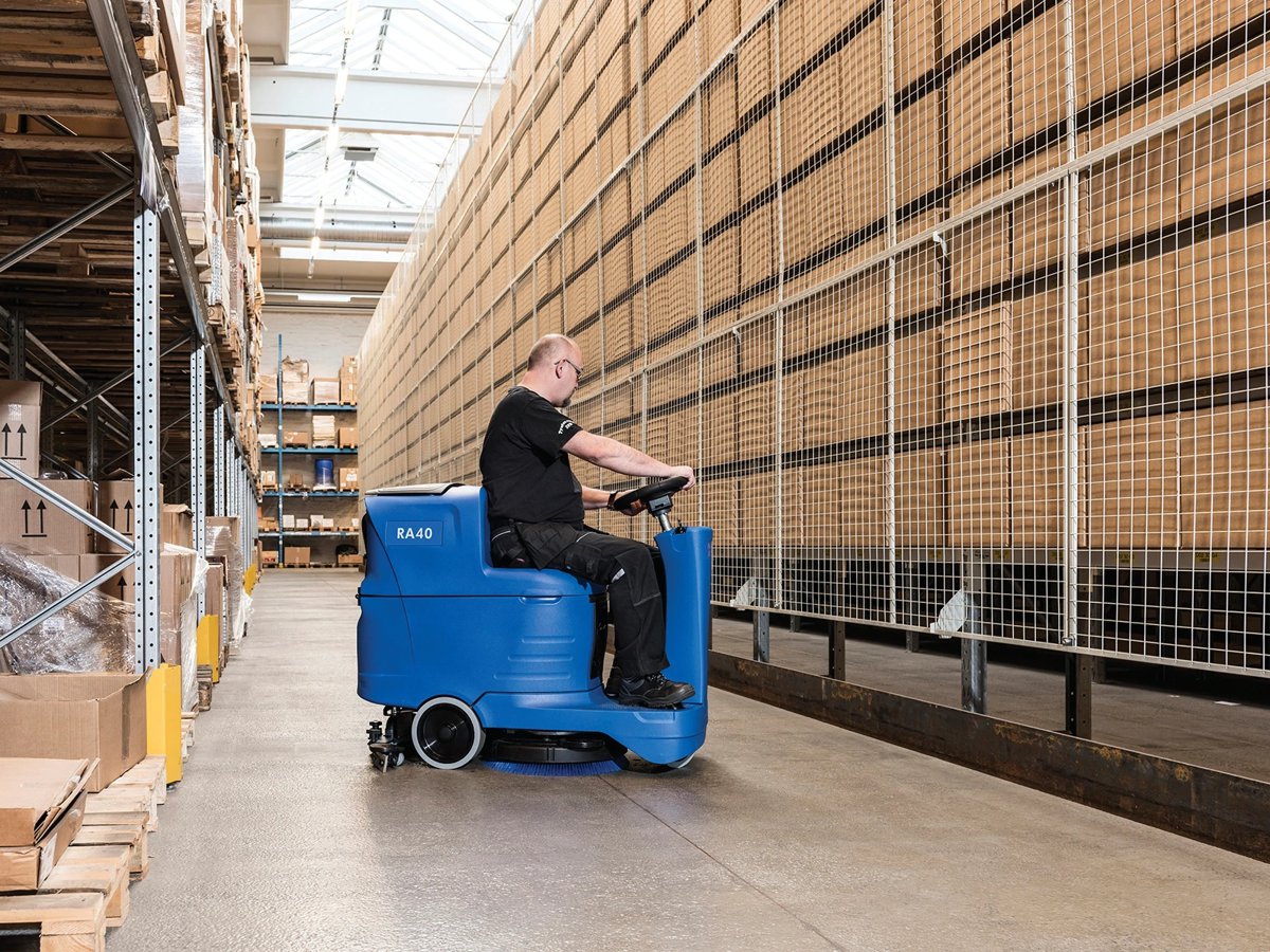 Operator scrubbing a warehouse aisle with a Clarke RA40 micro rider