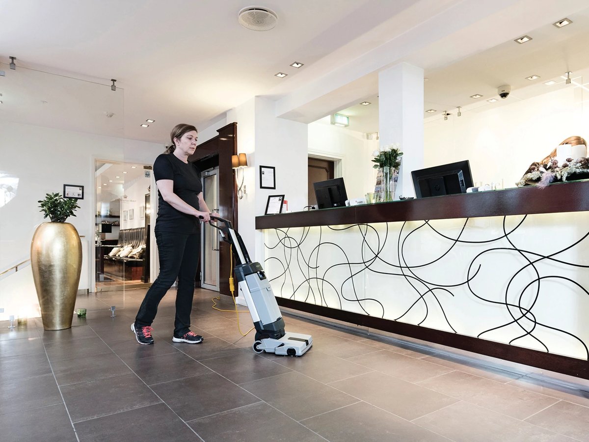 Cleaner scrubbing a hotel lobby floor with an Advance SC100