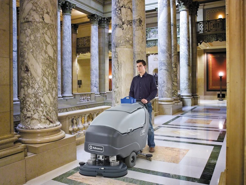 Operator using an Advance SC750 walk-behind scrubber on a marble floor in a public building