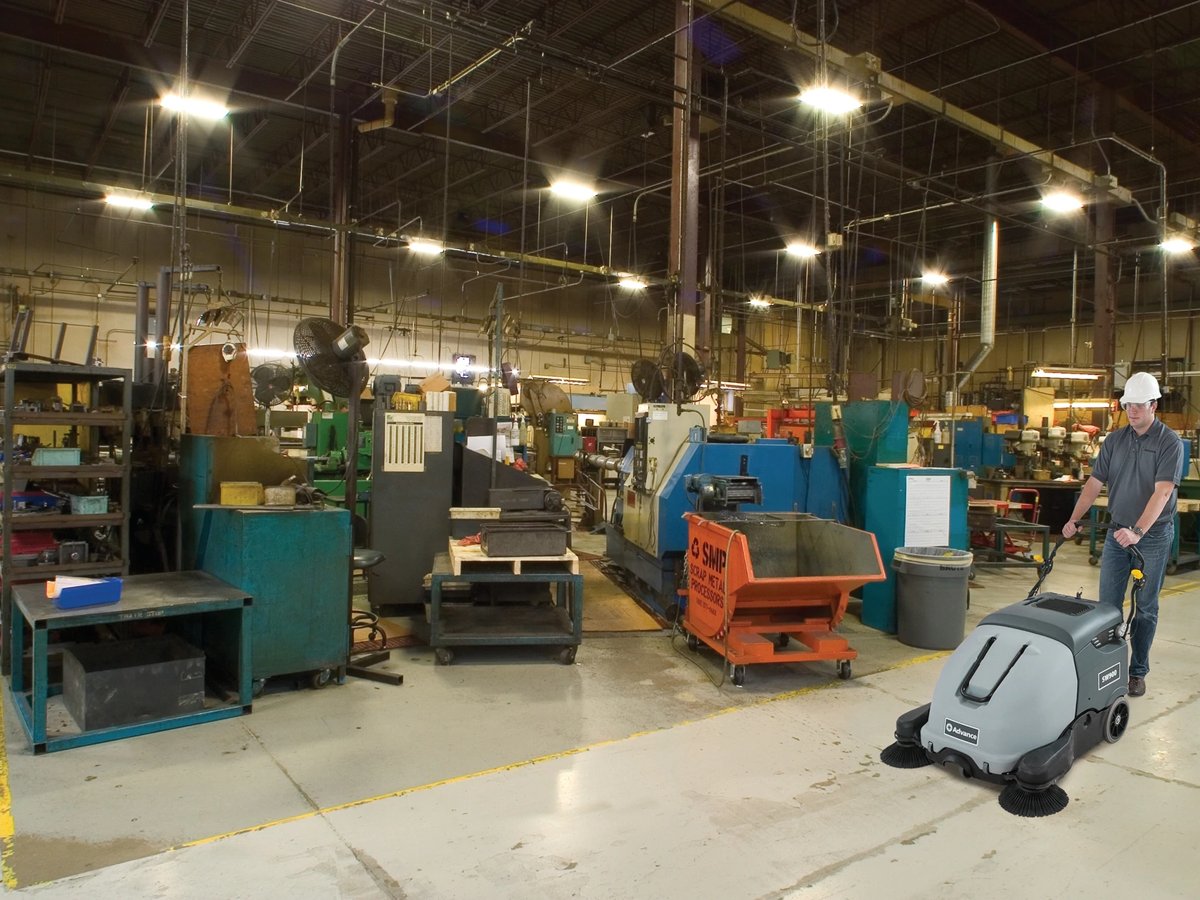 Operator sweeping a manufacturing floor with an Advance SW900 walk-behind sweeper