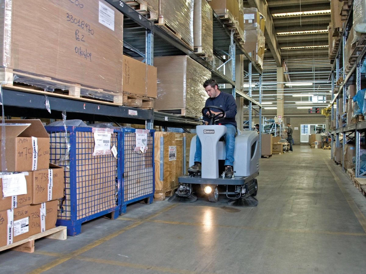 Operator sweeping a warehouse aisle on an Advance Terra 4300B rider sweeper