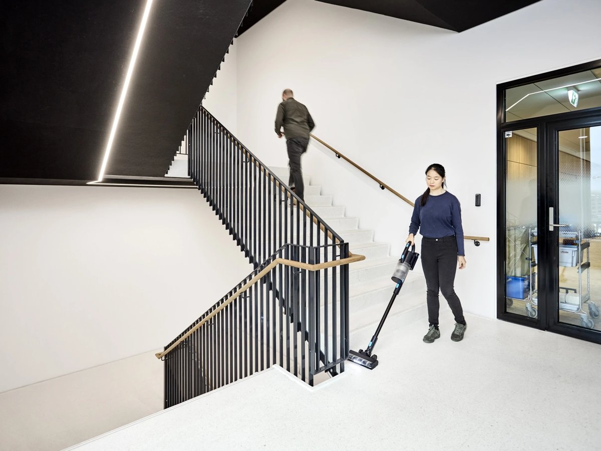 Cleaner using a Nilfisk VU200 cordless stick vacuum at the foot of a stairway