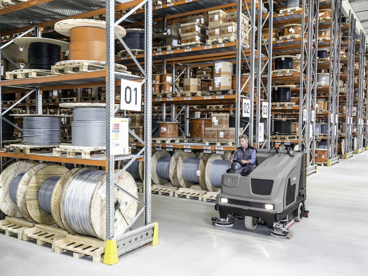 Operator driving a Kärcher B 300 R I down a warehouse aisle lined with cable reels