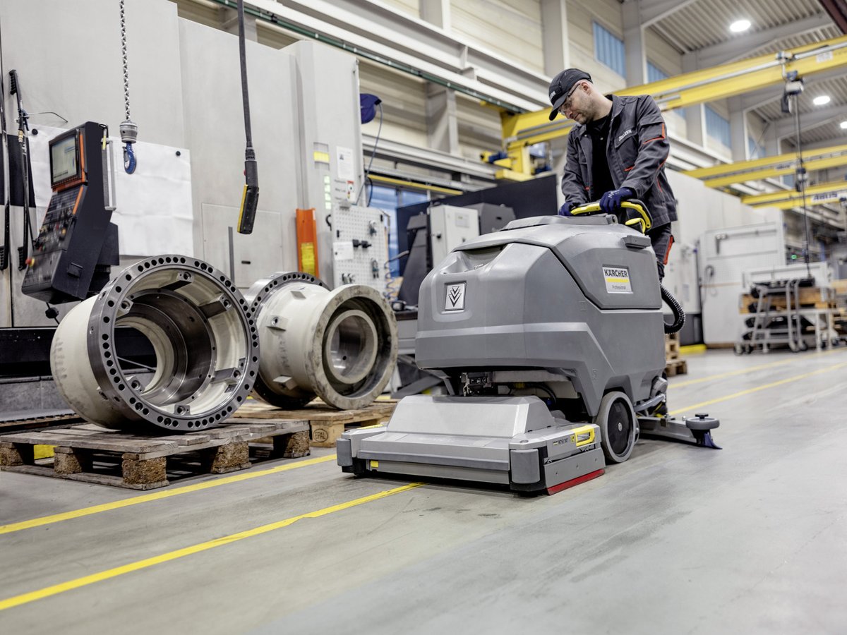 Worker scrubbing a factory floor beside machine parts with a Kärcher BR 75/75 W Bp Classic