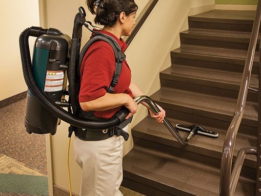 Operator wearing a Nobles Aspen-6 backpack vacuum while vacuuming stairs