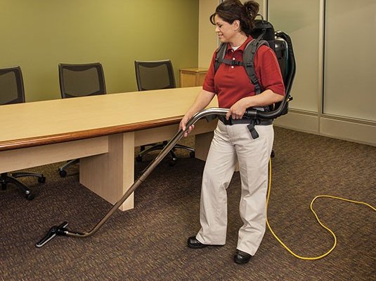 Operator using a Nobles Aspen-6 backpack vacuum on carpet in a conference room