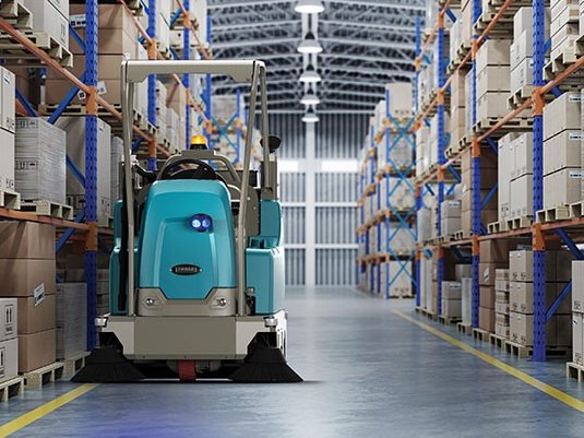 Tennant S16 ride-on sweeper with overhead guard sweeping a warehouse aisle