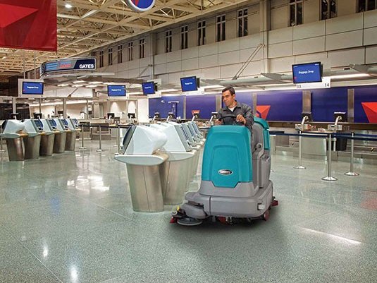 Operator scrubbing an airport terminal floor with a Tennant T12 rider scrubber