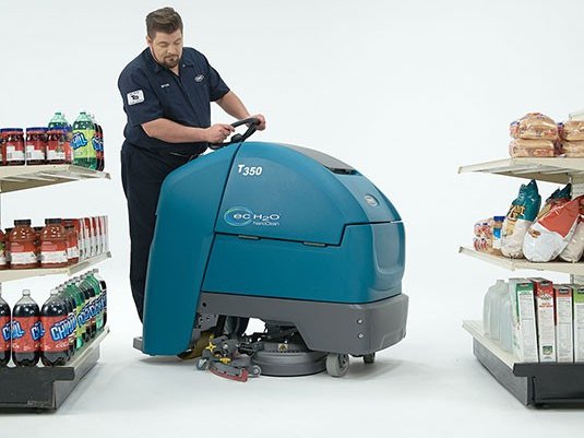 Operator scrubbing a store aisle with a Tennant T350 stand-on scrubber