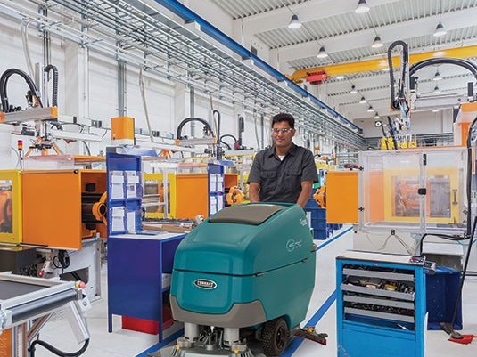 Operator scrubbing a manufacturing plant floor with a Tennant T600e