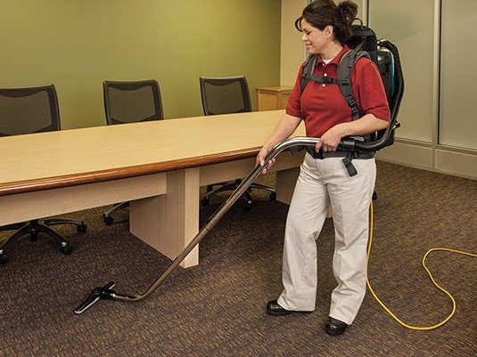 Operator vacuuming a conference room with a Tennant V-BP-6 backpack vacuum