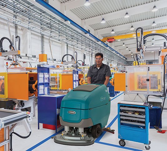 Tennant T600e walk-behind scrubber cleaning a manufacturing plant floor